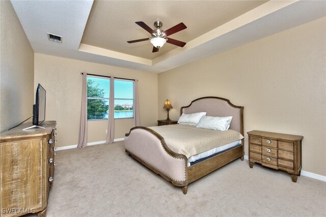 bedroom with a raised ceiling, ceiling fan, and light carpet