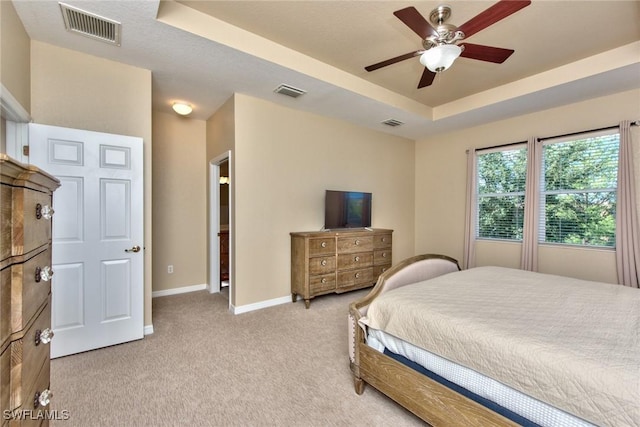 bedroom with ceiling fan, light colored carpet, and a tray ceiling