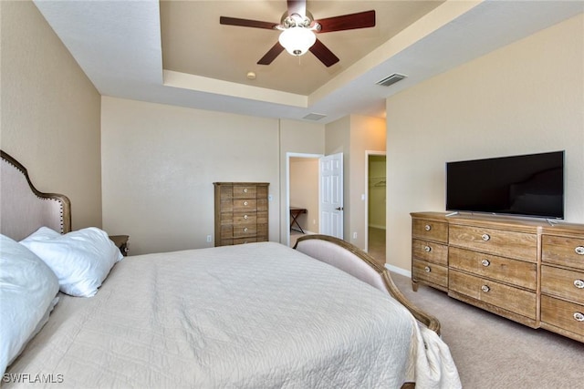 bedroom featuring a closet, light colored carpet, a tray ceiling, a walk in closet, and ceiling fan