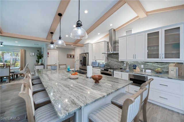 kitchen featuring vaulted ceiling with beams, hanging light fixtures, stainless steel appliances, light stone countertops, and wall chimney exhaust hood