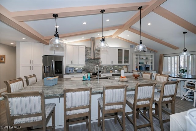 kitchen featuring decorative light fixtures, lofted ceiling with beams, white cabinetry, stainless steel fridge, and a kitchen bar