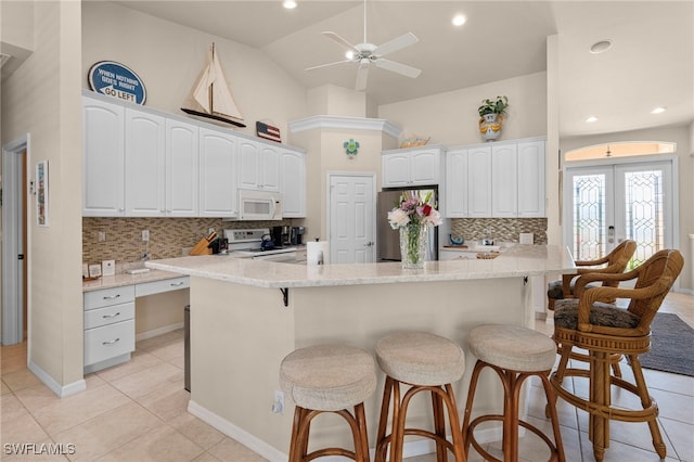 kitchen featuring french doors, light stone counters, white appliances, white cabinetry, and a breakfast bar area