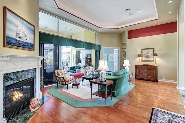 living room featuring wood-type flooring, a raised ceiling, and a high end fireplace