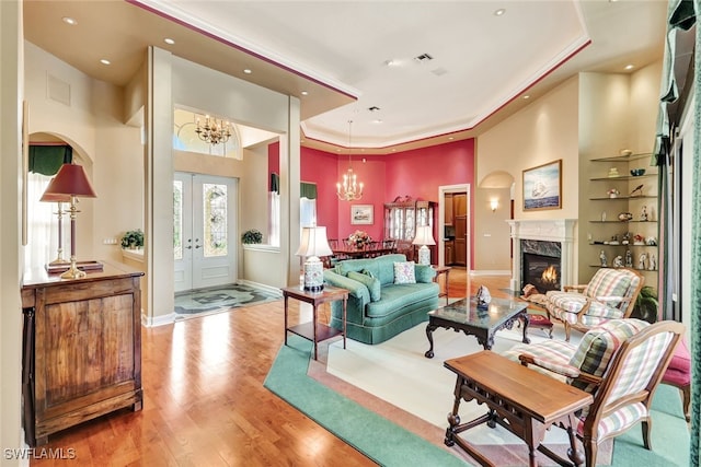 living room with light hardwood / wood-style floors, a notable chandelier, a fireplace, a tray ceiling, and built in shelves