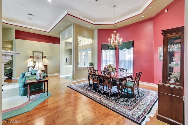 dining space featuring light wood-type flooring, an inviting chandelier, and a tray ceiling