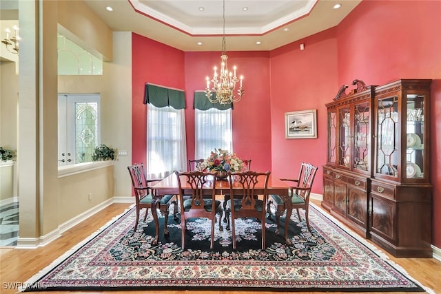 dining room featuring a raised ceiling, a chandelier, light hardwood / wood-style floors, and ornamental molding