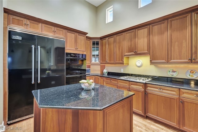 kitchen with stainless steel gas stovetop, built in fridge, a center island, and dark stone countertops