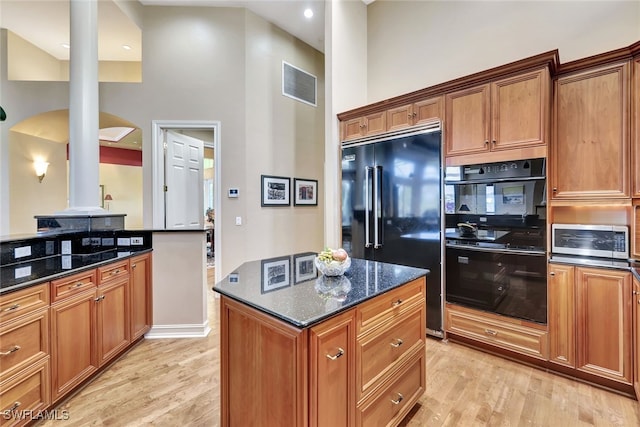 kitchen with a high ceiling, dark stone countertops, black appliances, and light hardwood / wood-style flooring