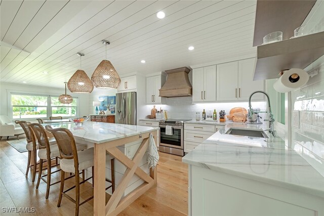 kitchen featuring stainless steel appliances, white cabinetry, hanging light fixtures, and custom exhaust hood