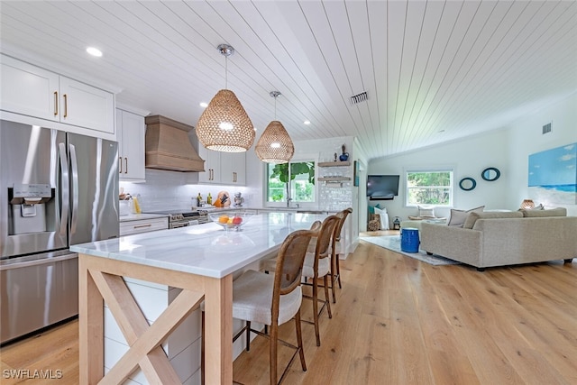 kitchen with stainless steel appliances, a kitchen island, premium range hood, white cabinets, and wood ceiling