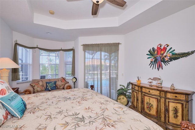 bedroom with ceiling fan, access to exterior, multiple windows, and a raised ceiling