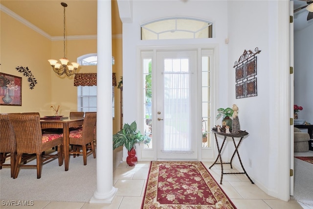 foyer entrance with a notable chandelier, light tile patterned flooring, ornamental molding, and decorative columns