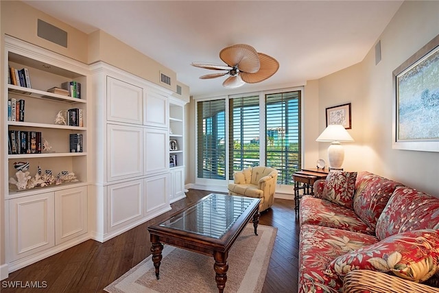 living room featuring ceiling fan, built in shelves, and dark wood-type flooring