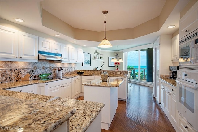 kitchen featuring pendant lighting, a center island, white appliances, white cabinets, and light stone counters