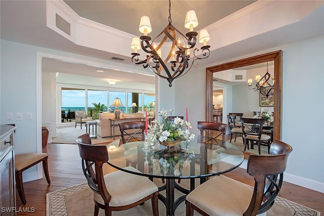 dining area with dark hardwood / wood-style flooring, ornamental molding, a raised ceiling, and an inviting chandelier