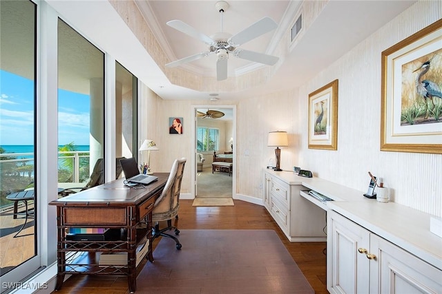 office area with built in desk, dark wood-type flooring, ornamental molding, ceiling fan, and a tray ceiling