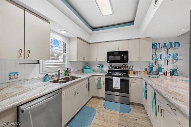 kitchen featuring sink, stainless steel appliances, light stone countertops, and a tray ceiling