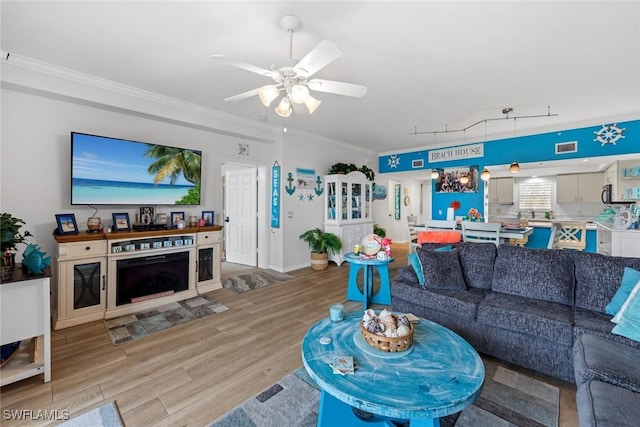 living room featuring light wood-type flooring, ceiling fan, and ornamental molding