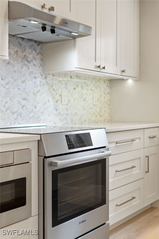 kitchen with tasteful backsplash, white cabinetry, oven, and light wood-type flooring