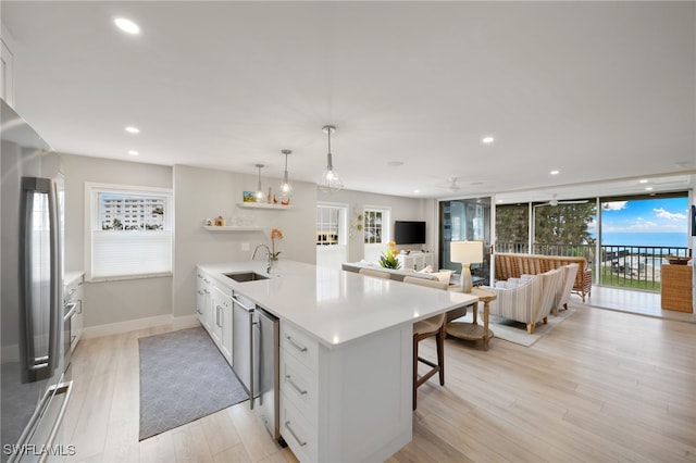 kitchen featuring stainless steel refrigerator, decorative light fixtures, sink, white cabinets, and a kitchen bar