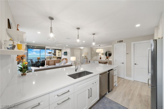 kitchen with appliances with stainless steel finishes, sink, white cabinets, hanging light fixtures, and light wood-type flooring