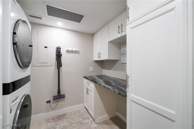 laundry area with stacked washer / dryer, electric panel, and cabinets