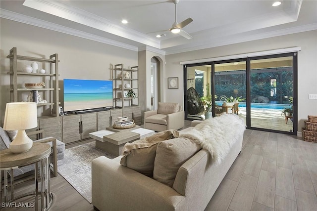 living room with hardwood / wood-style flooring, ceiling fan, crown molding, and a raised ceiling