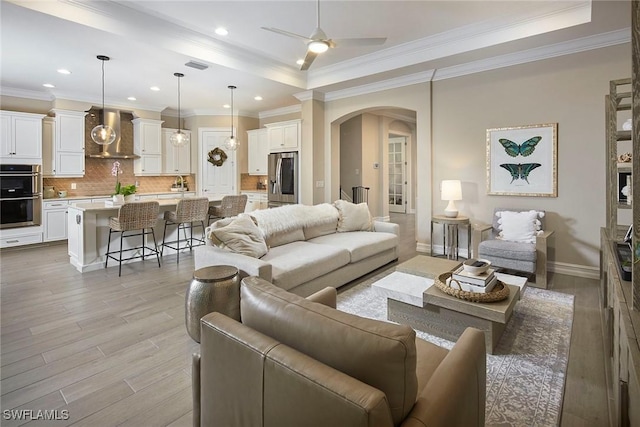 living room with ceiling fan, crown molding, a tray ceiling, and light hardwood / wood-style flooring