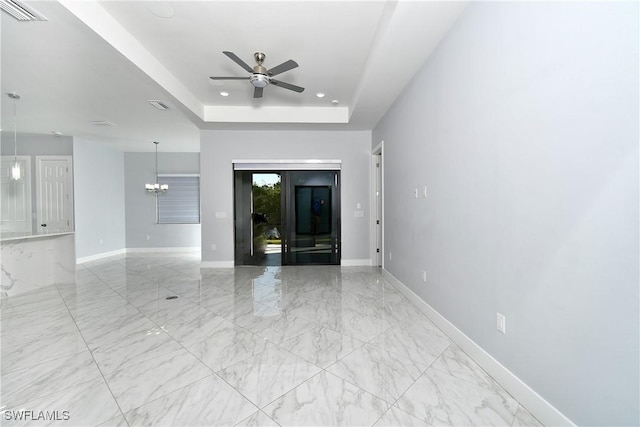 unfurnished living room with a raised ceiling and ceiling fan with notable chandelier