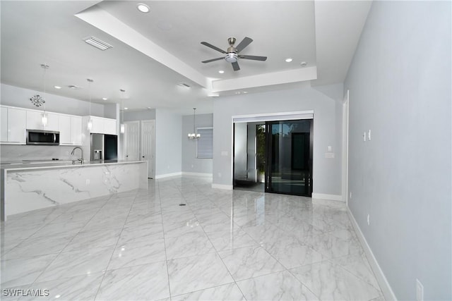 unfurnished living room with sink, a raised ceiling, and ceiling fan with notable chandelier