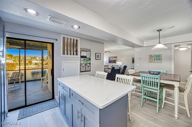 kitchen featuring a center island, decorative light fixtures, light stone counters, and gray cabinetry