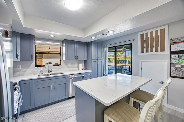 kitchen featuring a kitchen breakfast bar, a raised ceiling, sink, stainless steel dishwasher, and a kitchen island