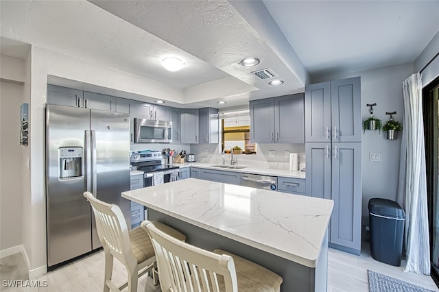 kitchen featuring a breakfast bar, sink, light stone countertops, a kitchen island, and stainless steel appliances