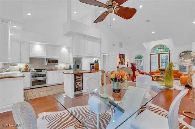 dining area featuring ceiling fan, sink, light wood-type flooring, high vaulted ceiling, and beverage cooler