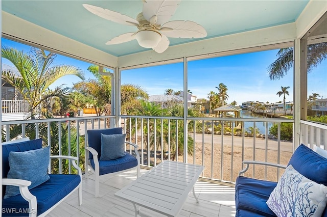 sunroom with ceiling fan and a water view