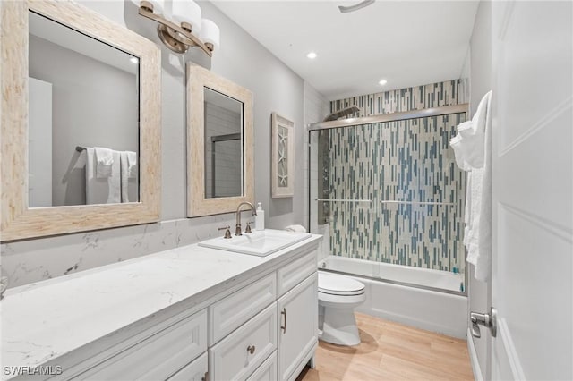 full bathroom featuring shower / bath combination with glass door, vanity, hardwood / wood-style flooring, and toilet