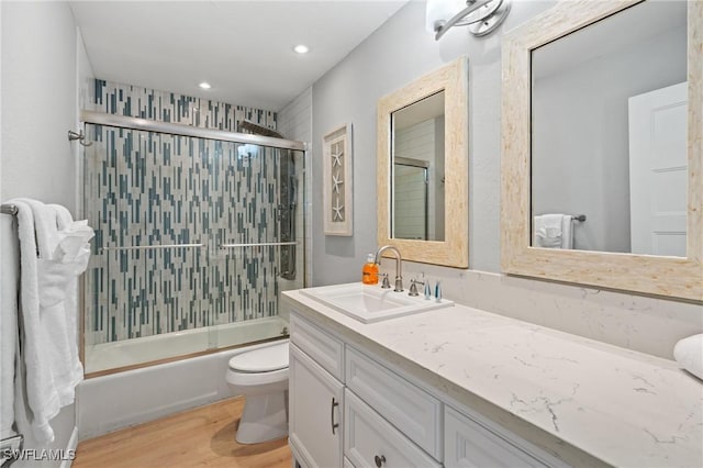 full bath featuring toilet, wood finished floors, recessed lighting, bath / shower combo with glass door, and vanity