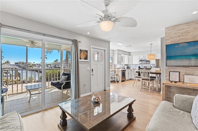 living room with ceiling fan, a water view, and light wood-type flooring