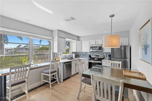 kitchen featuring white cabinets, tasteful backsplash, decorative light fixtures, light hardwood / wood-style floors, and stainless steel appliances