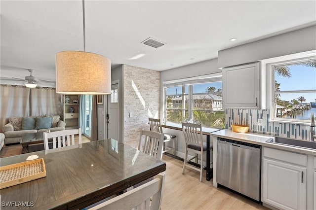 kitchen featuring dishwasher, a water view, tasteful backsplash, decorative light fixtures, and white cabinetry