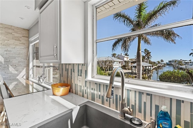 interior details with white cabinets, decorative backsplash, a water view, and light stone counters