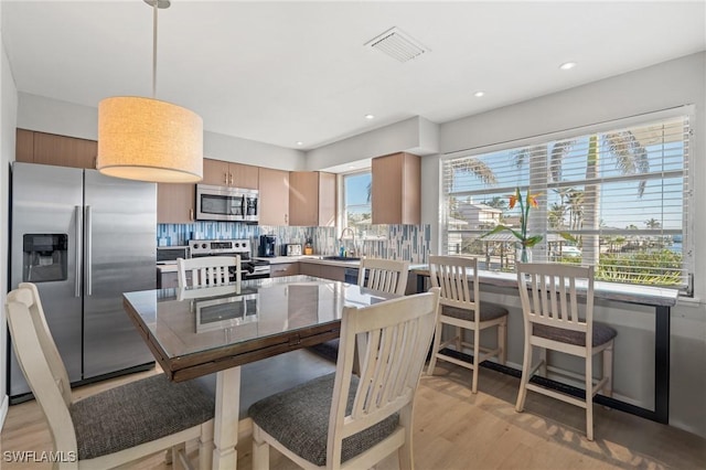 kitchen featuring light wood-type flooring, tasteful backsplash, stainless steel appliances, sink, and decorative light fixtures