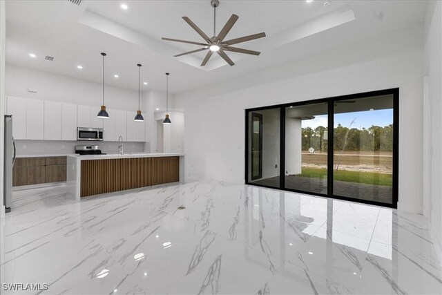 kitchen with a raised ceiling, a kitchen island with sink, white cabinetry, and stainless steel appliances