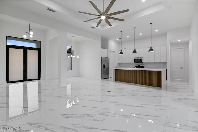 kitchen featuring pendant lighting, white cabinets, a tray ceiling, stainless steel appliances, and a spacious island