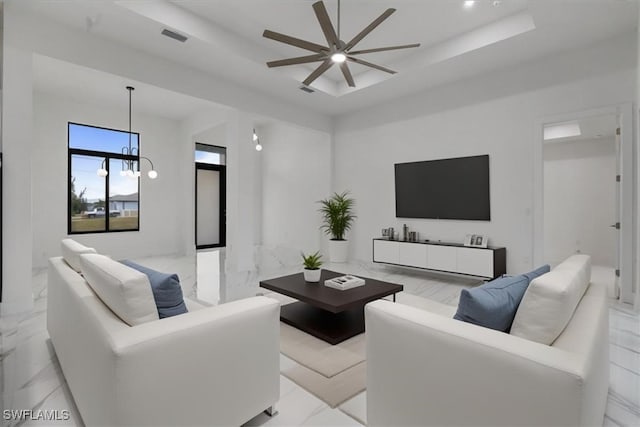 living room with ceiling fan with notable chandelier and a tray ceiling