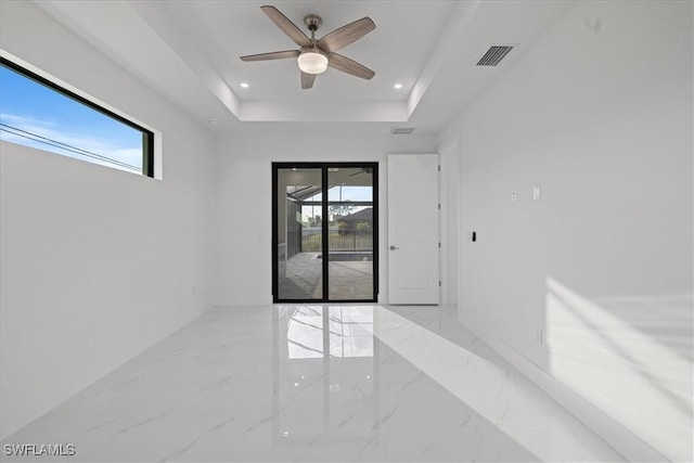 unfurnished room featuring ceiling fan, a tray ceiling, and a wealth of natural light