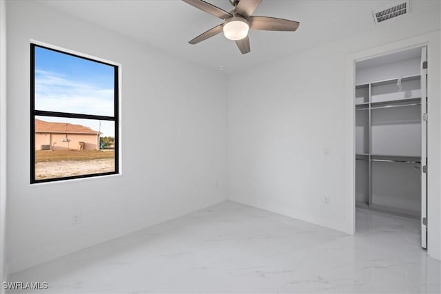 unfurnished bedroom featuring a walk in closet, a closet, and ceiling fan