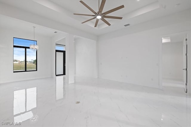 unfurnished room with ceiling fan with notable chandelier and a raised ceiling