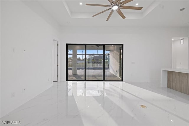 empty room featuring a high ceiling, ceiling fan, and a tray ceiling