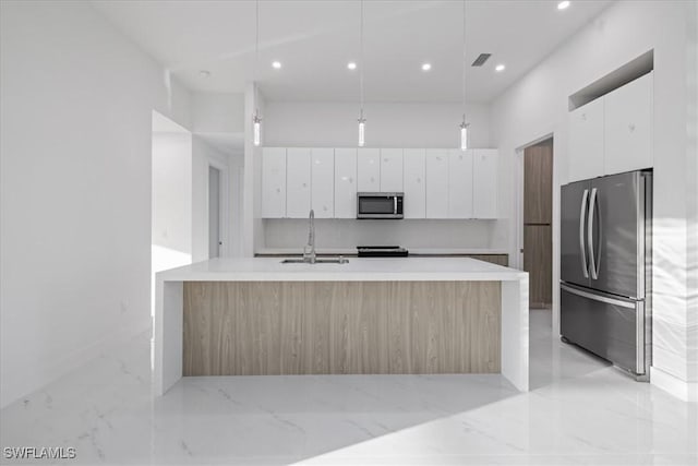 kitchen with sink, white cabinetry, hanging light fixtures, appliances with stainless steel finishes, and a kitchen island with sink